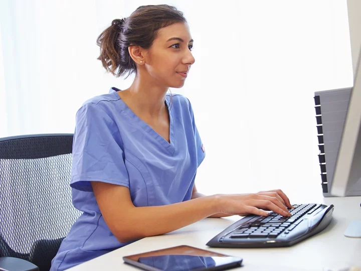 Female Nurse In Office Working At Computer