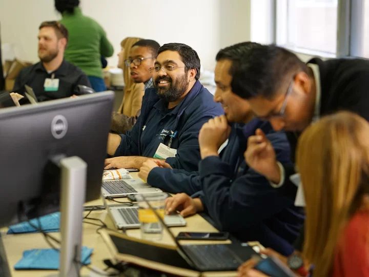 A diverse group of individuals diligently working on computers in a well-lit classroom setting.