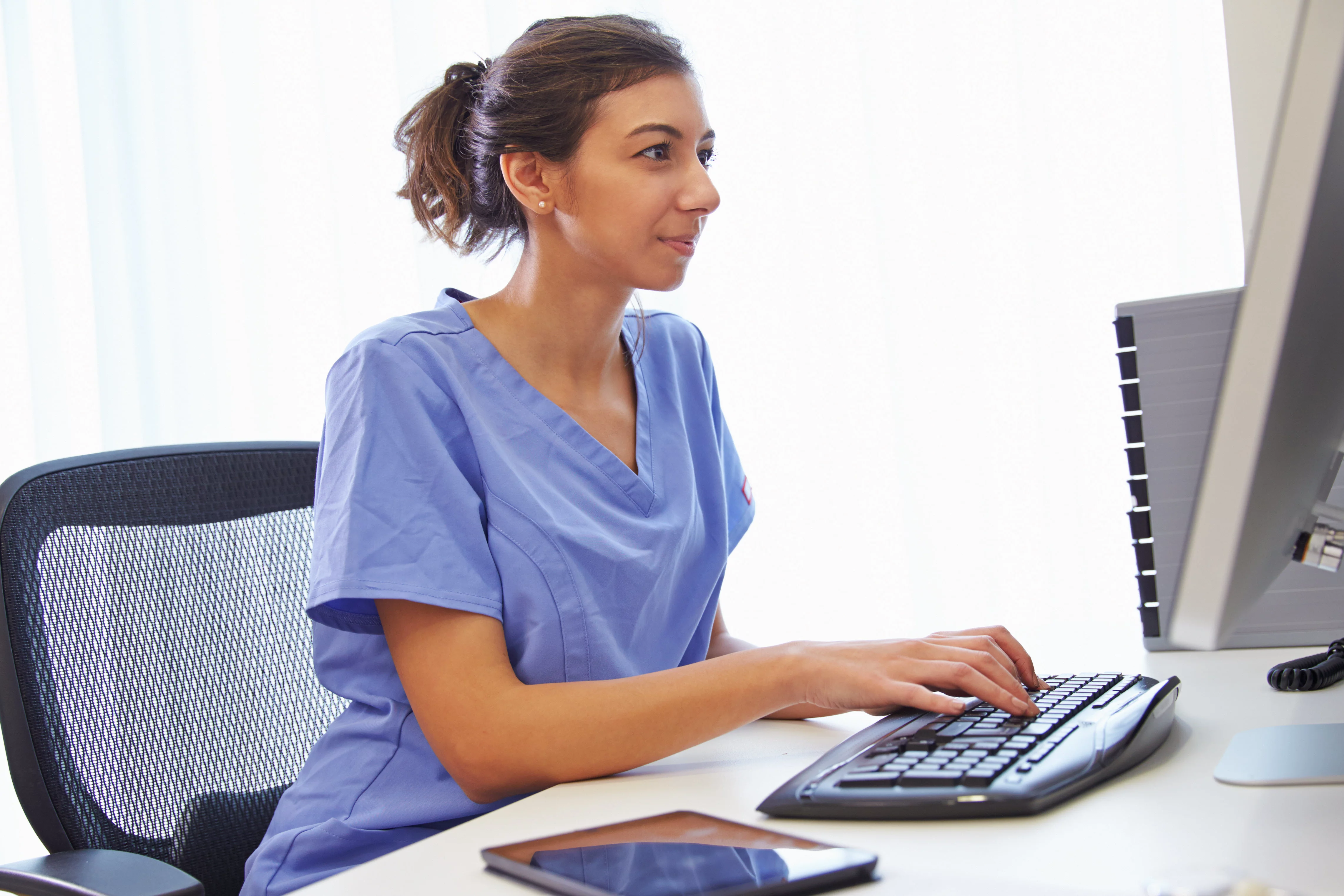 Female Nurse In Office Working At Computer